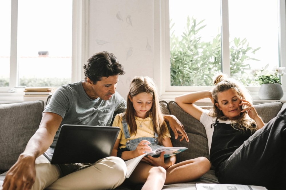 Familie i sofaen med PC, nettbrett og blad.