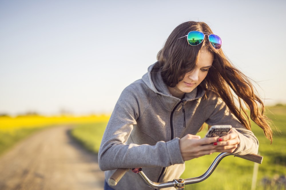 Ung dame med sykkel som har stoppa og tastar på mobilen.