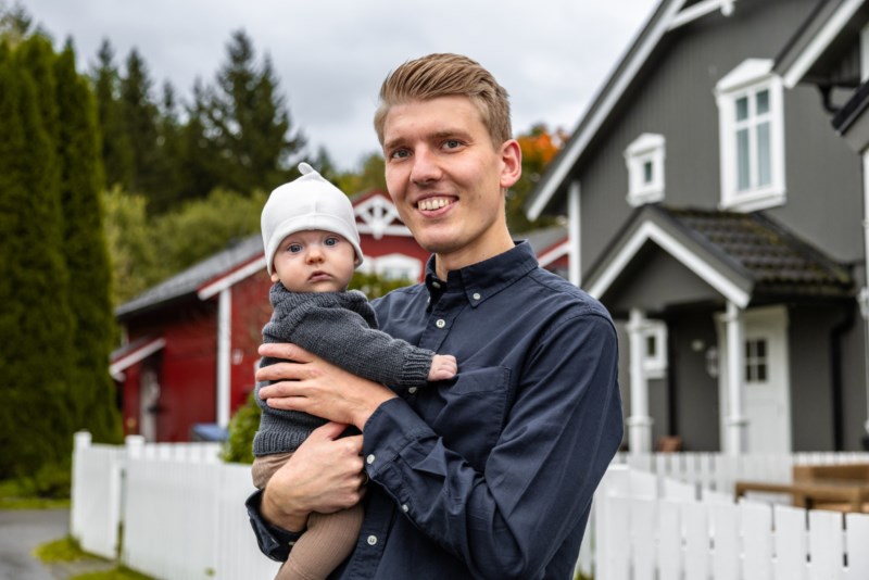 Ung familiefar med baby utanfor grått hus