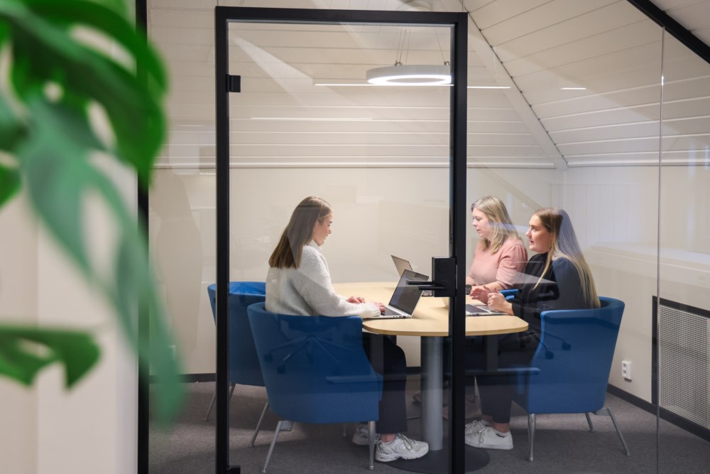 Tre jenter ved eit møtebord i eit glasskontor.