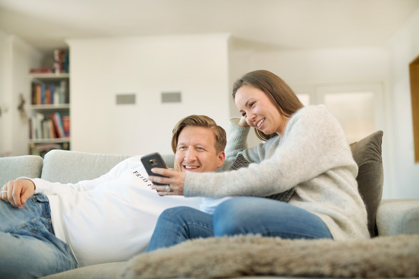 Smilande mann og kvinne som sit i ein sofa og ser på ei bærbar datamaskin